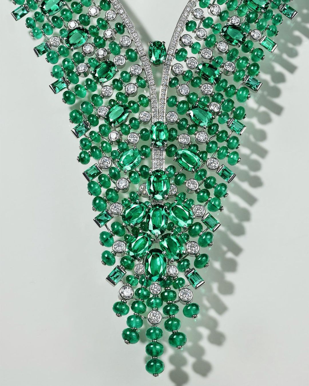 Emerald and diamond cascade necklace on a white background. Close-up of luxury jewelry with green and white gemstones.