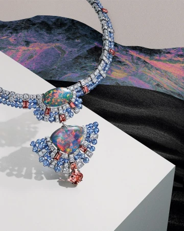 Elegant necklace with opal pendant, set with sapphires and diamonds, displayed against a background featuring both a textured drapery and mountain