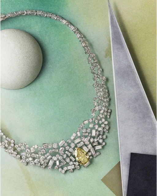 Elegant diamond necklace with a yellow central stone, set on a green watercolor paper background with geometric shapes.
