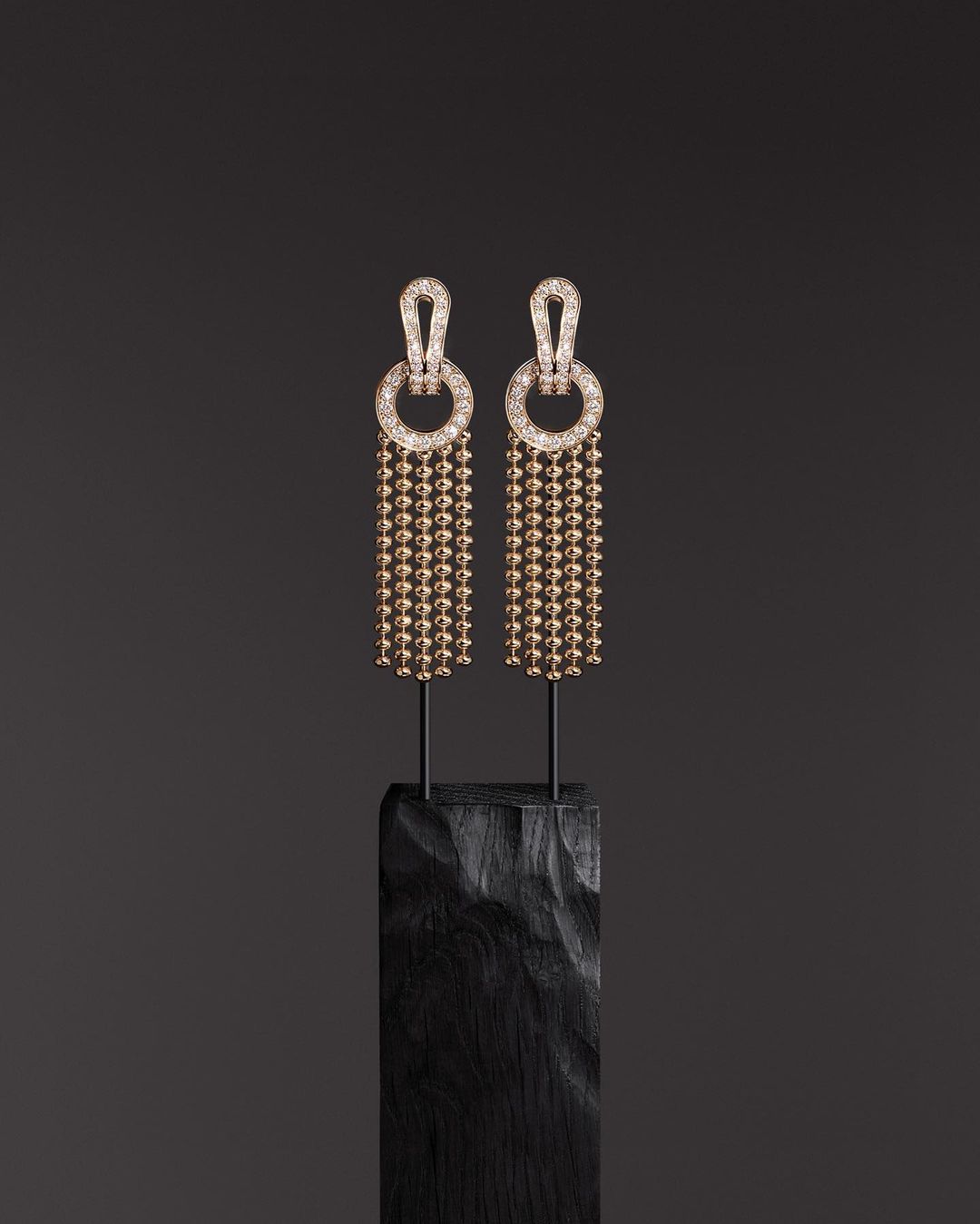 Elegant pair of drop earrings with spherical beads on dark textured stand against a dark grey backdrop, highlighting jewelry craftsmanship.