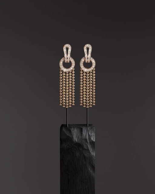Elegant pair of drop earrings with spherical beads on dark textured stand against a dark grey backdrop, highlighting jewelry craftsmanship.