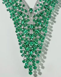 Close-up of an elaborate diamond and emerald necklace featuring clusters of green beads and faceted gems against a plain white background.