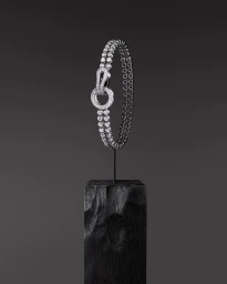 Diamond tennis bracelet on a black stand against a dark grey seamless background