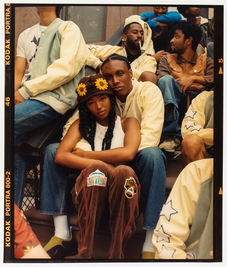 Group of stylish people in vintage-inspired clothing, posing on steps in an urban setting with a film camera border effect.