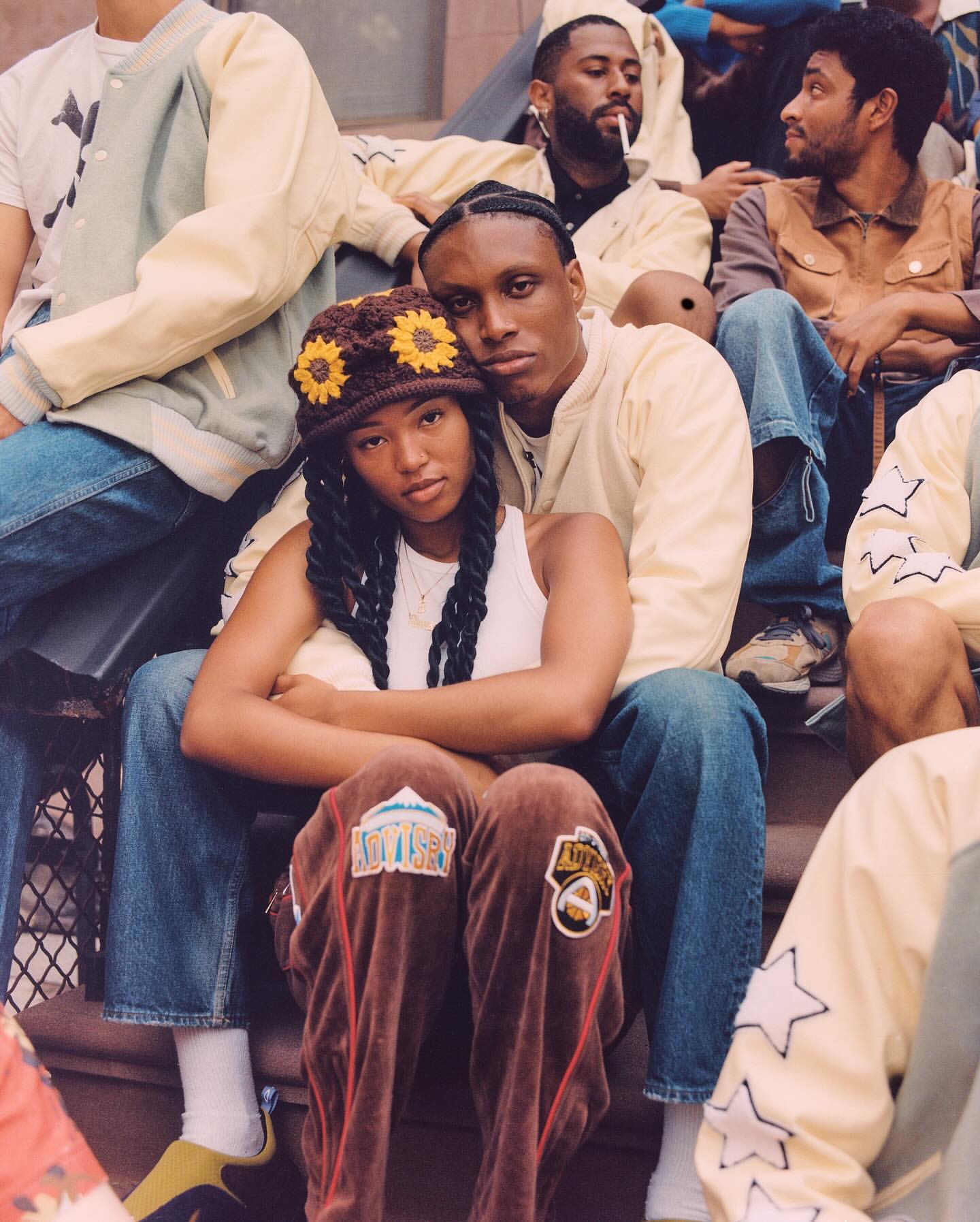 Group of fashionable young adults in outdoor setting wearing stylish jackets, jeans, hats, pants and shoes in an outdoor scene.