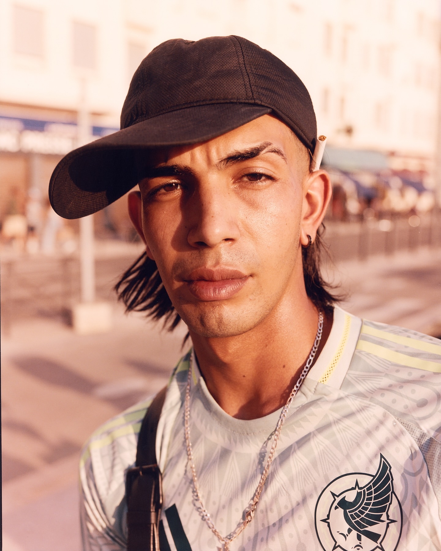 Portrait of a young adult man wearing a cap and sports jersey, close up in natural outdoor lighting with a shallow depth of field.