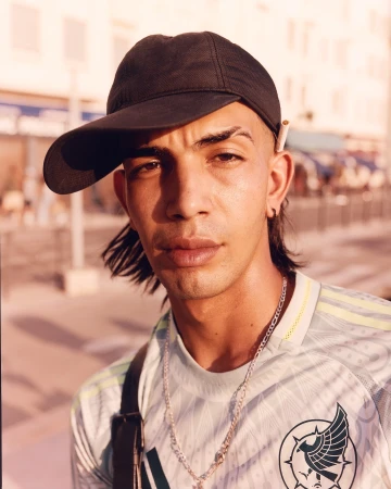 Portrait of a young adult man wearing a cap and sports jersey, close up in natural outdoor lighting with a shallow depth of field.