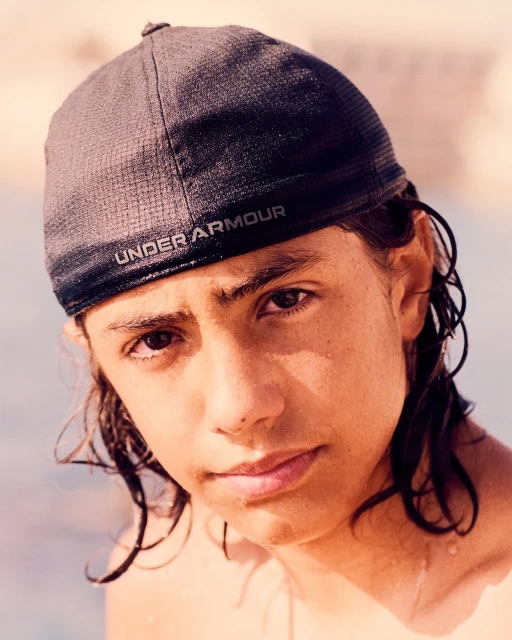 Portrait of a young adult with dark hair wearing a baseball cap outdoors, focusing on the face and expression.