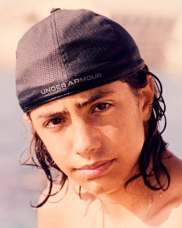 Portrait of a young adult with dark hair wearing a baseball cap outdoors, focusing on the face and expression.