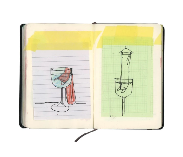Open sketchbook displaying line art drawings of wine glasses on graph paper, affixed with yellow tape on a white backdrop.