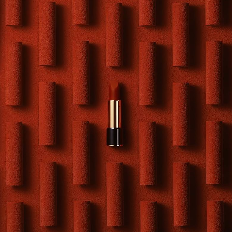 Close-up of a red lipstick tube surrounded by a textured red background with multiple indistinct cylinders creating a pattern.