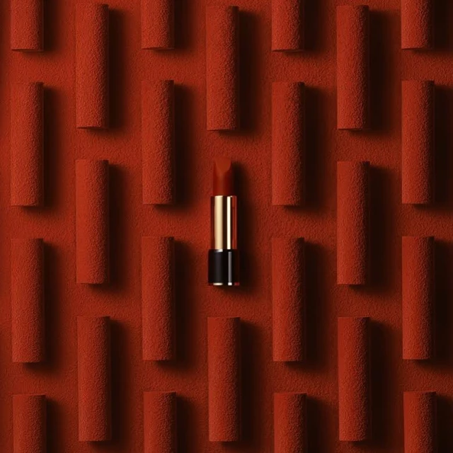 Close-up of a red lipstick tube surrounded by a textured red background with multiple indistinct cylinders creating a pattern.