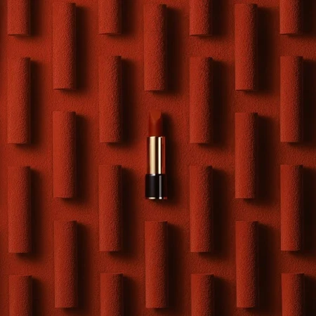 Close-up of a red lipstick tube surrounded by a textured red background with multiple indistinct cylinders creating a pattern.