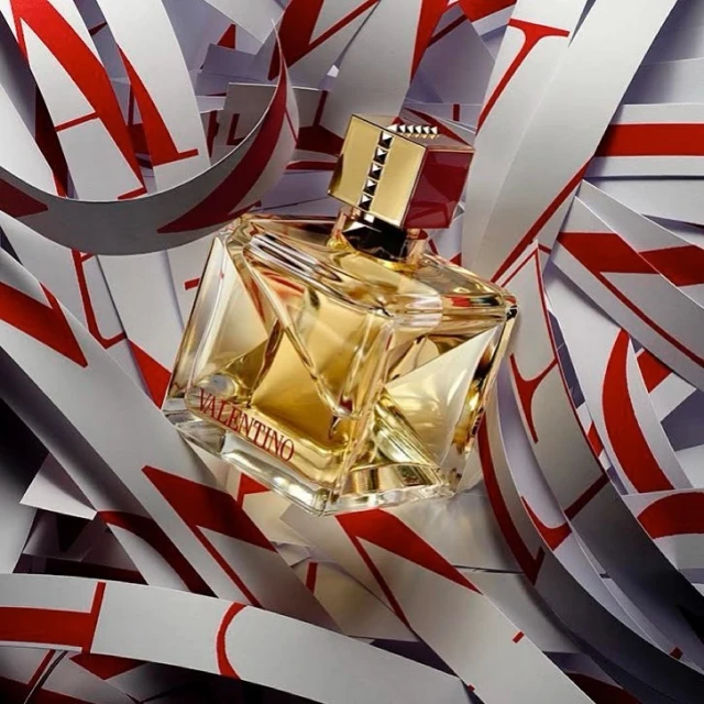 Valentino perfume bottle sits among swirling paper cutouts of the brand's logo, showcasing a beauty product in a studio setting.