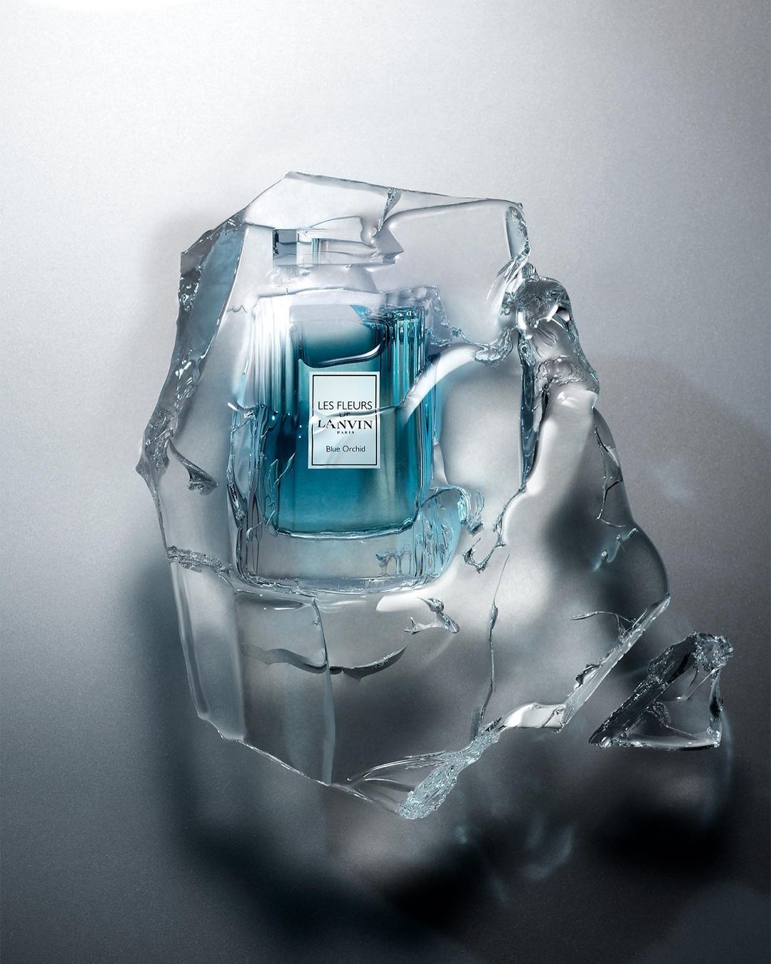 Fragrance bottle by Lanvin encased in a block of clear, cracked ice, set against a soft grey background, highlighting its unique presentation.