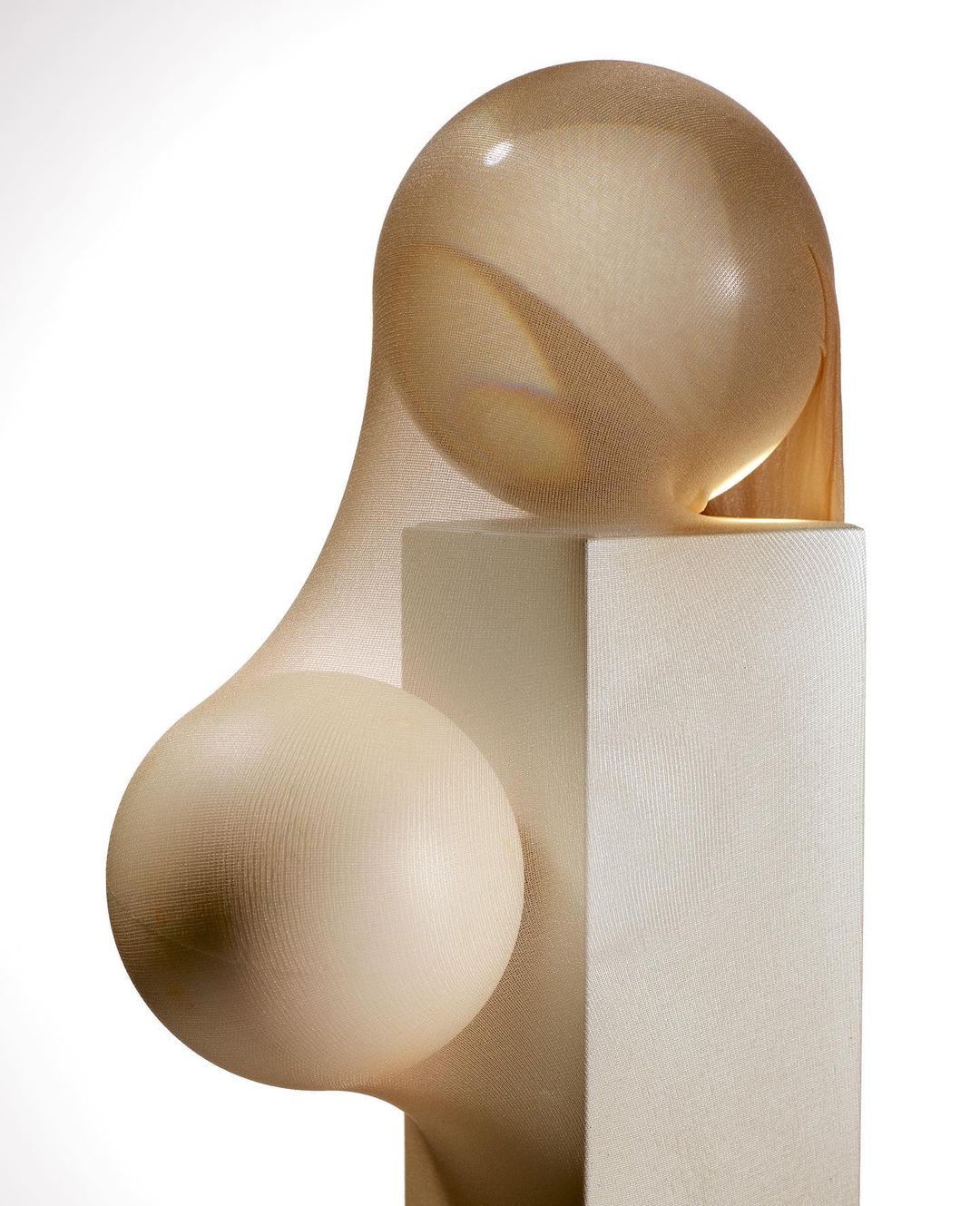 Abstract still life of spherical forms covered in sheer hosiery fabric atop a plinth in a studio setting with neutral color palette.