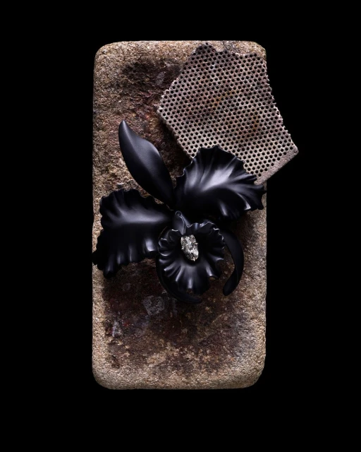 Still life shot of a black orchid jewelry piece on a stone surface, alongside a piece of patterned mesh, set against a dark background.