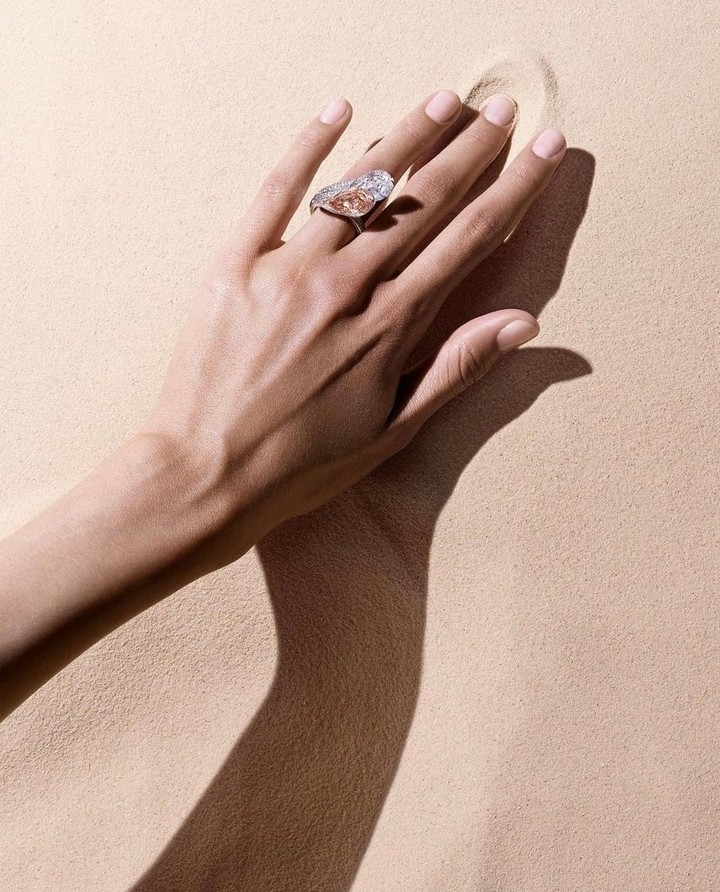 Elegant hand displays a ring with a large, pear-shaped diamond in a minimalistic beige setting, highlighting jewelry details.