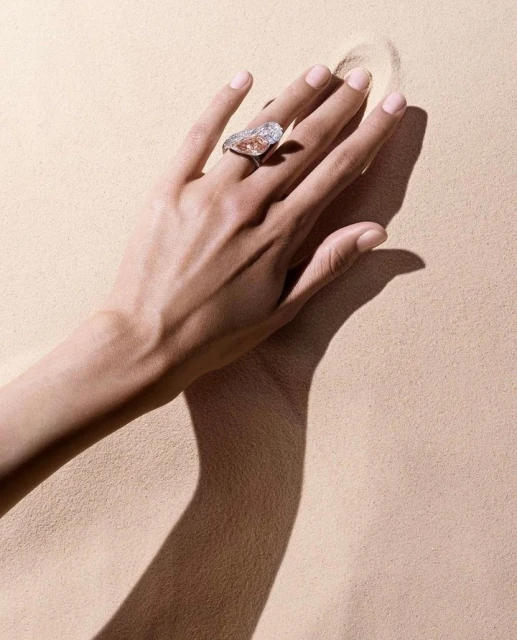 Elegant hand displays a ring with a large, pear-shaped diamond in a minimalistic beige setting, highlighting jewelry details.