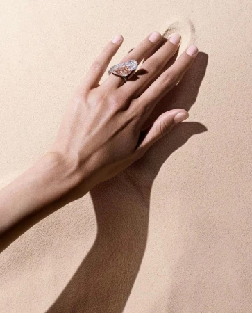 Elegant hand displays a ring with a large, pear-shaped diamond in a minimalistic beige setting, highlighting jewelry details.