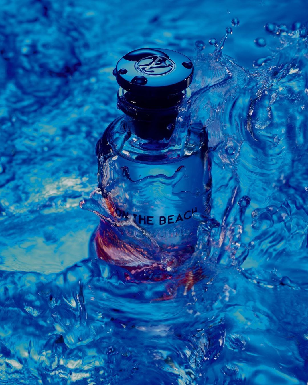 Perfume bottle with 'On the Beach' text on a blue background with splashing water, set against a monochromatic blue backdrop.