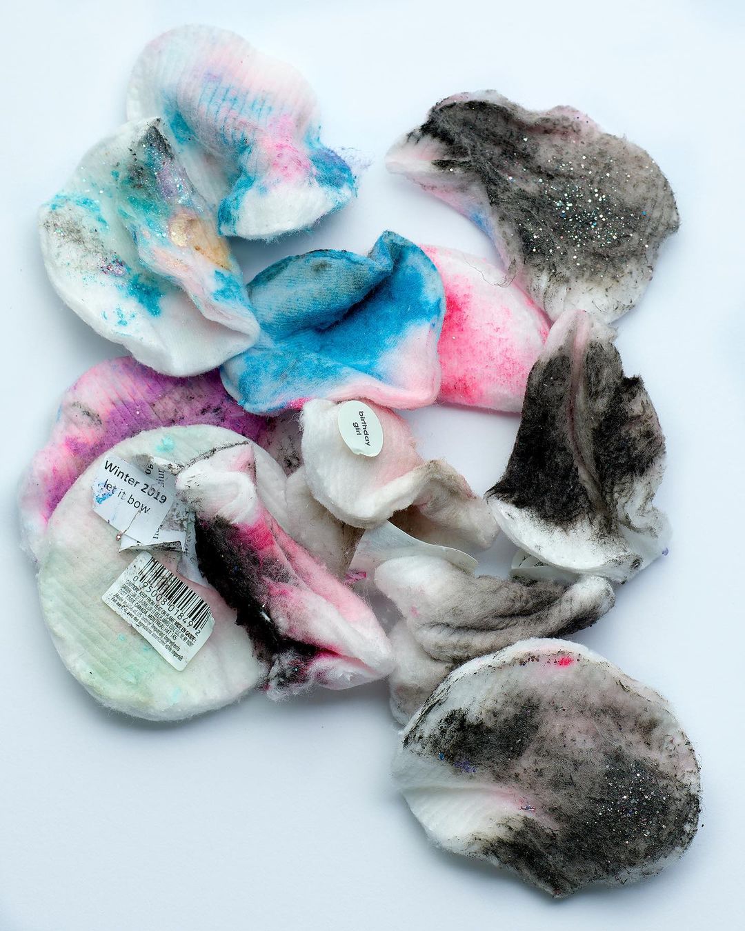 Close-up overhead shot of assorted pastel-colored petal-shaped makeup pads scattered on a white surface with soft lighting.