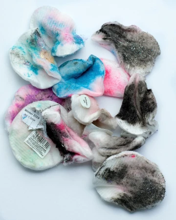 Close-up overhead shot of assorted pastel-colored petal-shaped makeup pads scattered on a white surface with soft lighting.