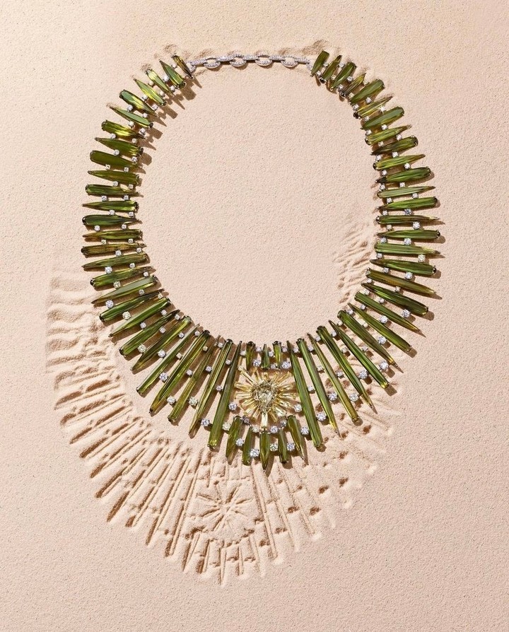 High-angle shot of a green and diamond necklace with a star-shaped center on a tan background, casting intricate shadows.