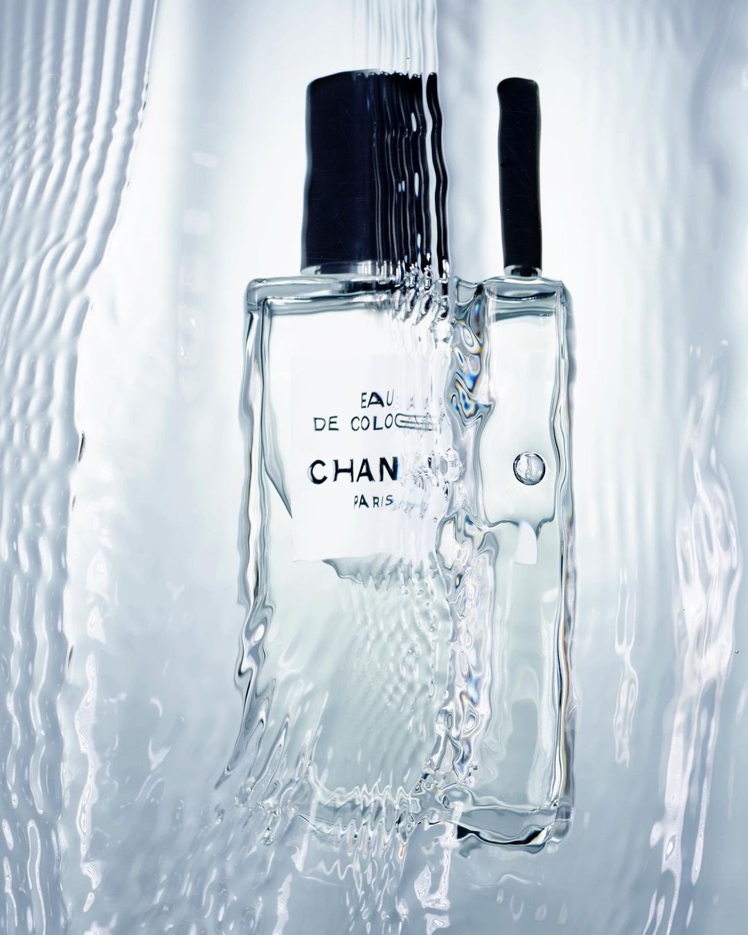 Clear Chanel cologne bottle with water cascading down, showcasing its minimalist design and creating a fresh, clean aesthetic.