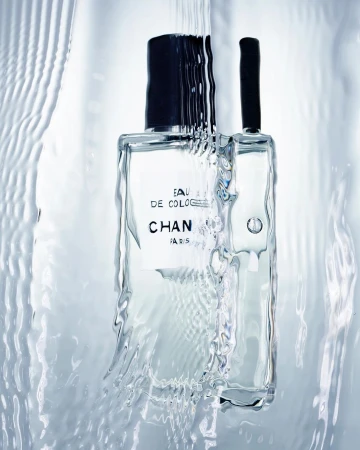Clear Chanel cologne bottle with water cascading down, showcasing its minimalist design and creating a fresh, clean aesthetic.