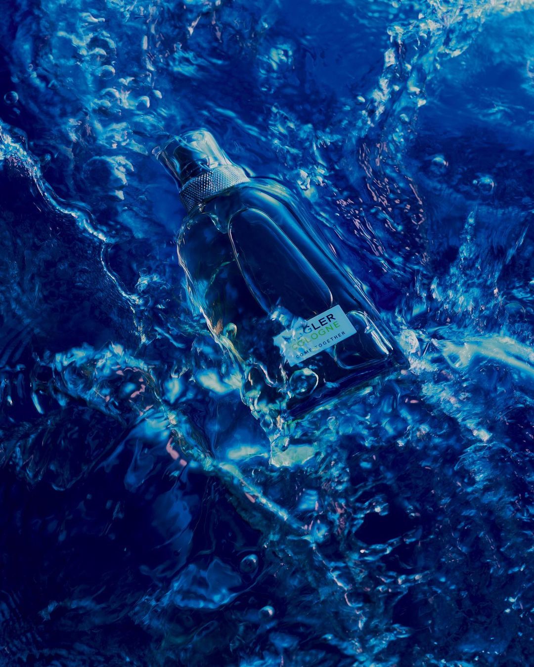 A glass bottle of cologne is submerged in vibrant blue water with light reflections, creating a refreshing and dynamic visual.