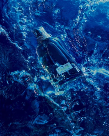 A glass bottle of cologne is submerged in vibrant blue water with light reflections, creating a refreshing and dynamic visual.