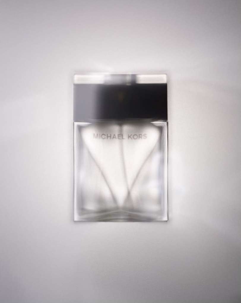 Michael Kors perfume bottle on a white surface, showcasing a modern glass design with a black cap and logo for the brand.