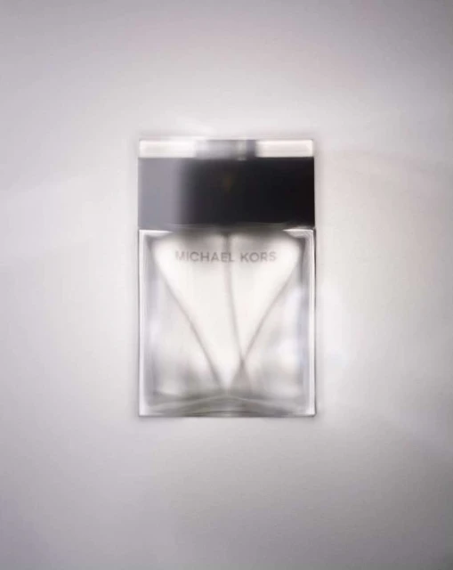 Michael Kors perfume bottle on a white surface, showcasing a modern glass design with a black cap and logo for the brand.