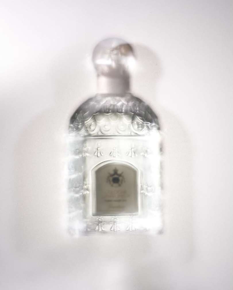 Elevated shot of a blurred, decorative glass perfume bottle with a round stopper on a white surface, suggesting an out-of-focus aesthetic.