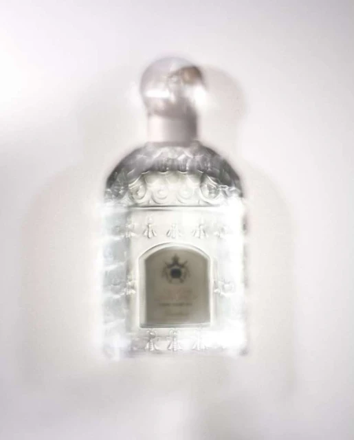 Elevated shot of a blurred, decorative glass perfume bottle with a round stopper on a white surface, suggesting an out-of-focus aesthetic.
