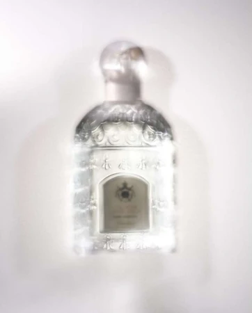 Elevated shot of a blurred, decorative glass perfume bottle with a round stopper on a white surface, suggesting an out-of-focus aesthetic.