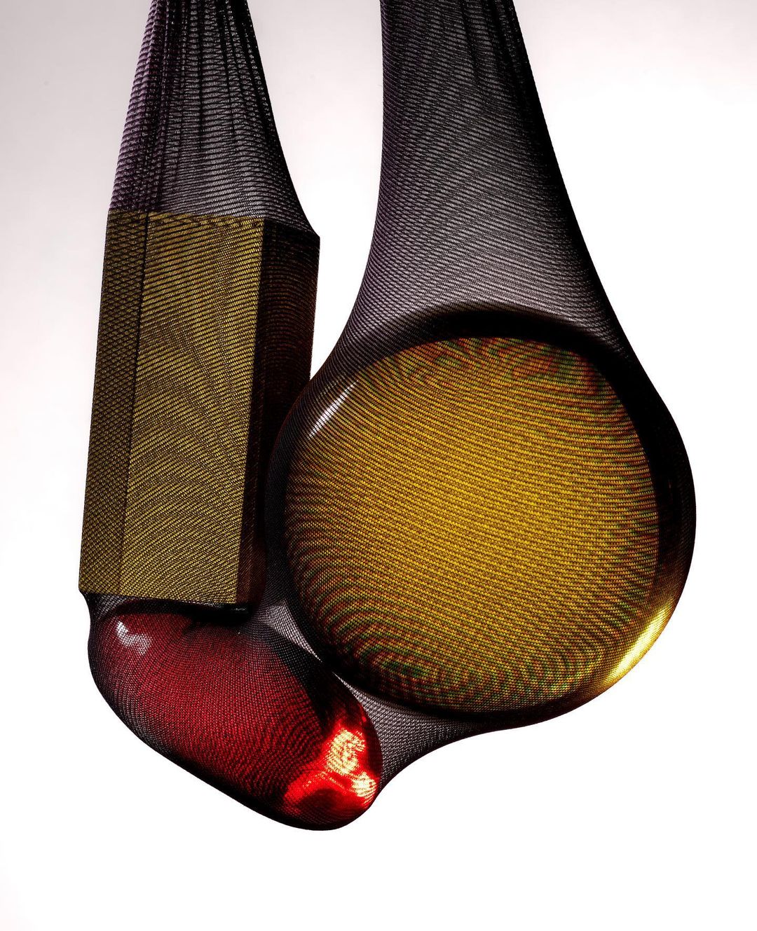 Three objects - a bronze hexagon, a bronze sphere, and a red capsule - suspended in black mesh against a gradient white background.