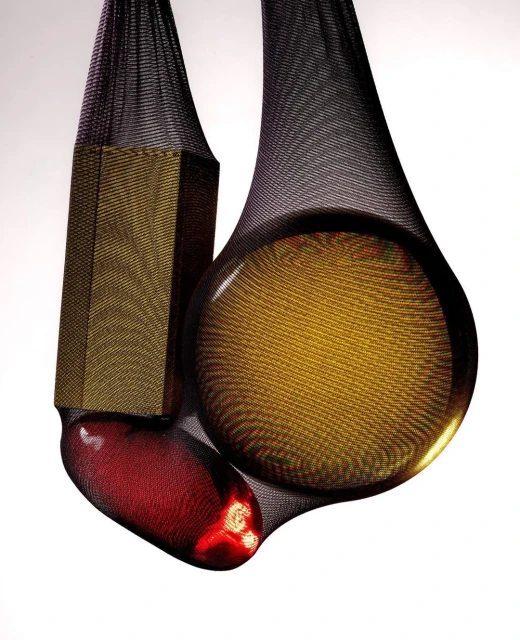 Three objects - a bronze hexagon, a bronze sphere, and a red capsule - suspended in black mesh against a gradient white background.