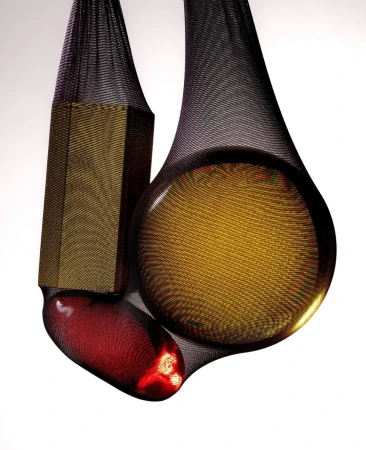 Three objects - a bronze hexagon, a bronze sphere, and a red capsule - suspended in black mesh against a gradient white background.