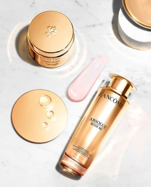 Still life product shot of Lancôme Absolue skincare products including a cream, serum, and applicator on a marble surface.