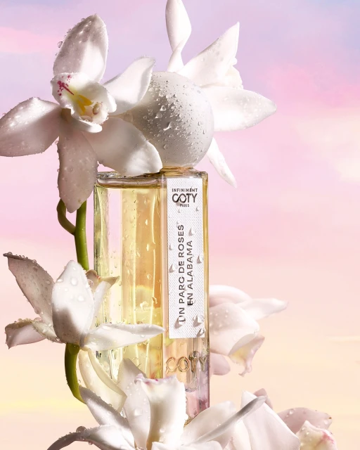 Coty fragrance bottle surrounded by white orchids. Product shot with a soft pink background. Beauty and fragrance advertising.
