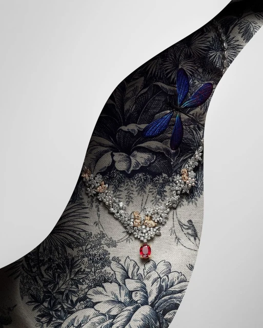 Elegant diamond necklace with a ruby pendant displayed against a botanical toile fabric and a gradient white backdrop in a jewellery advertisement.