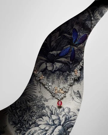 Elegant diamond necklace with a ruby pendant displayed against a botanical toile fabric and a gradient white backdrop in a jewellery advertisement.