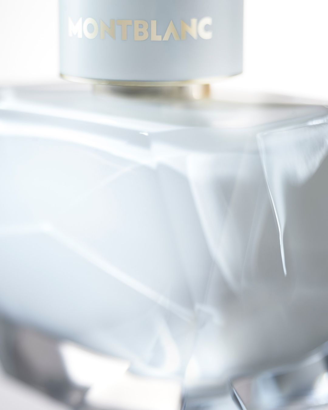 Close-up studio shot of a Montblanc fragrance bottle with a smooth, light-blue surface and gold lettering on a white background.