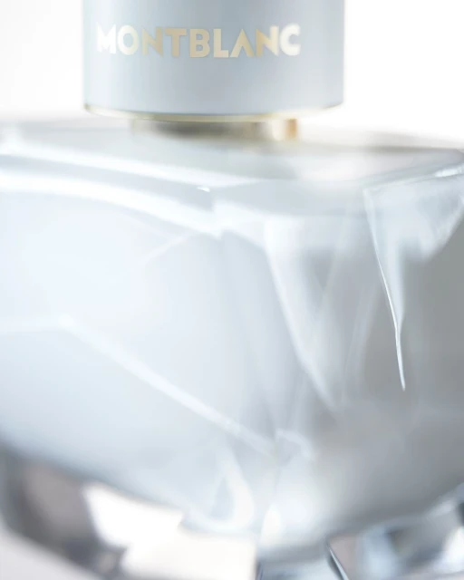 Close-up studio shot of a Montblanc fragrance bottle with a smooth, light-blue surface and gold lettering on a white background.