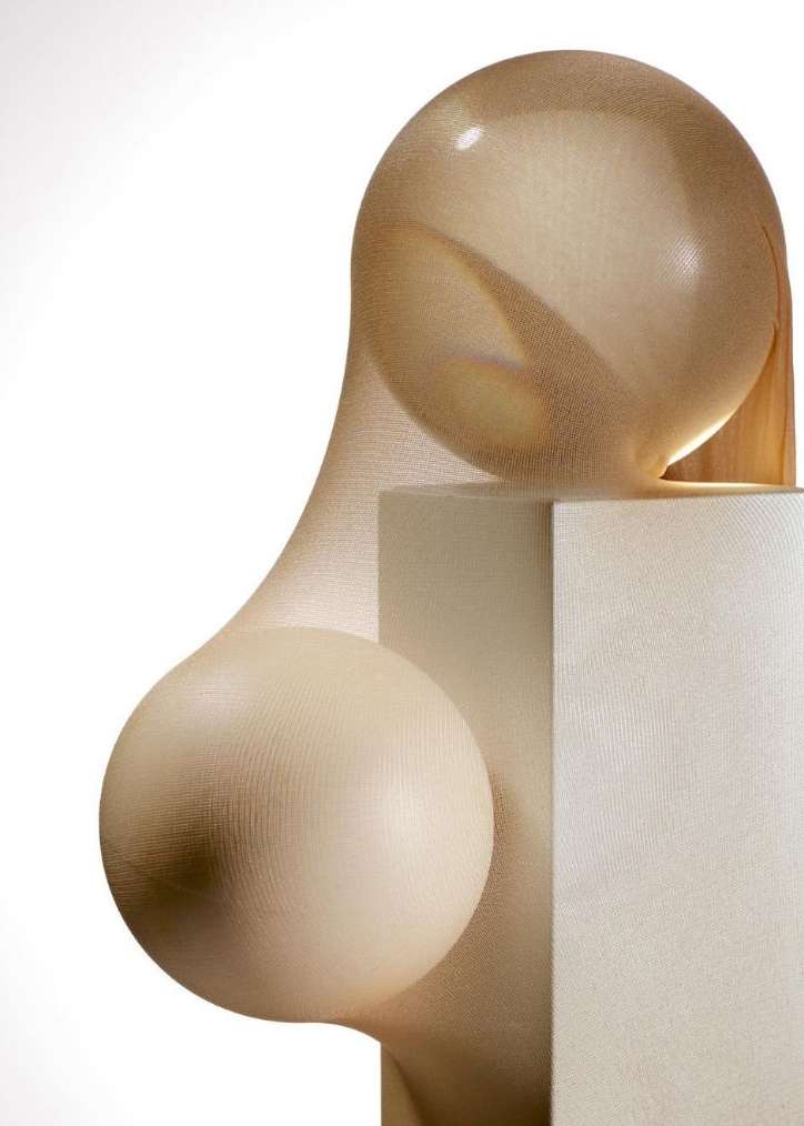 Tan sheer fabric stretches over spheres and a cube, creating an abstract form against a white background in a studio setting.