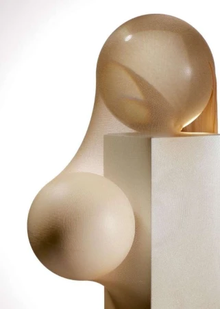 Tan sheer fabric stretches over spheres and a cube, creating an abstract form against a white background in a studio setting.