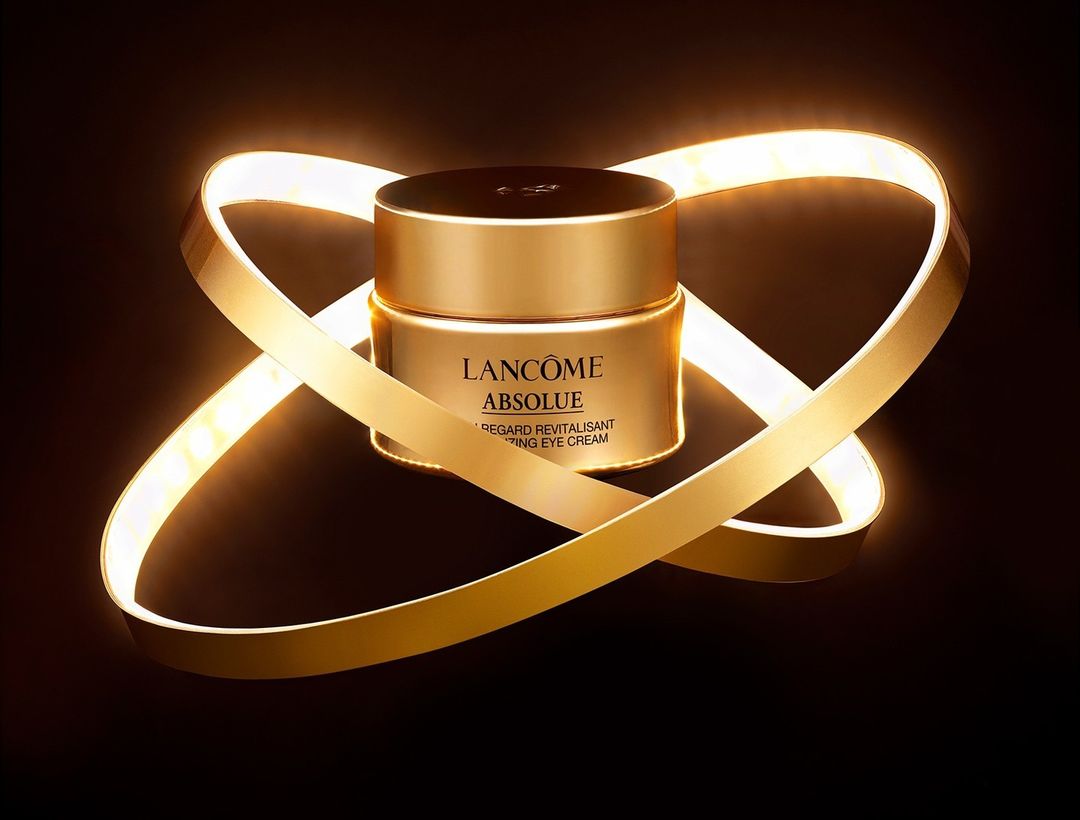 Gold Lancôme Absolue eye cream jar surrounded by a looping LED light on a black background. Beauty and skincare product.
