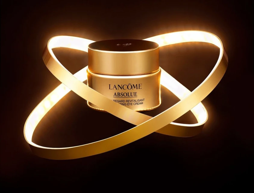 Gold Lancôme Absolue eye cream jar surrounded by a looping LED light on a black background. Beauty and skincare product.